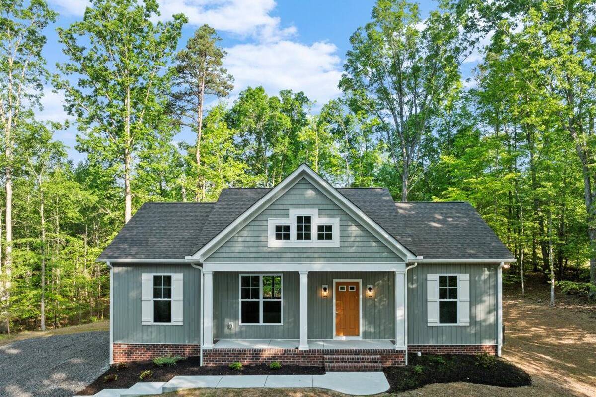 custom built craftsman home with brick foundation, stained wood door, shaker style shutters, large active dormer, white columns and landscaped yard