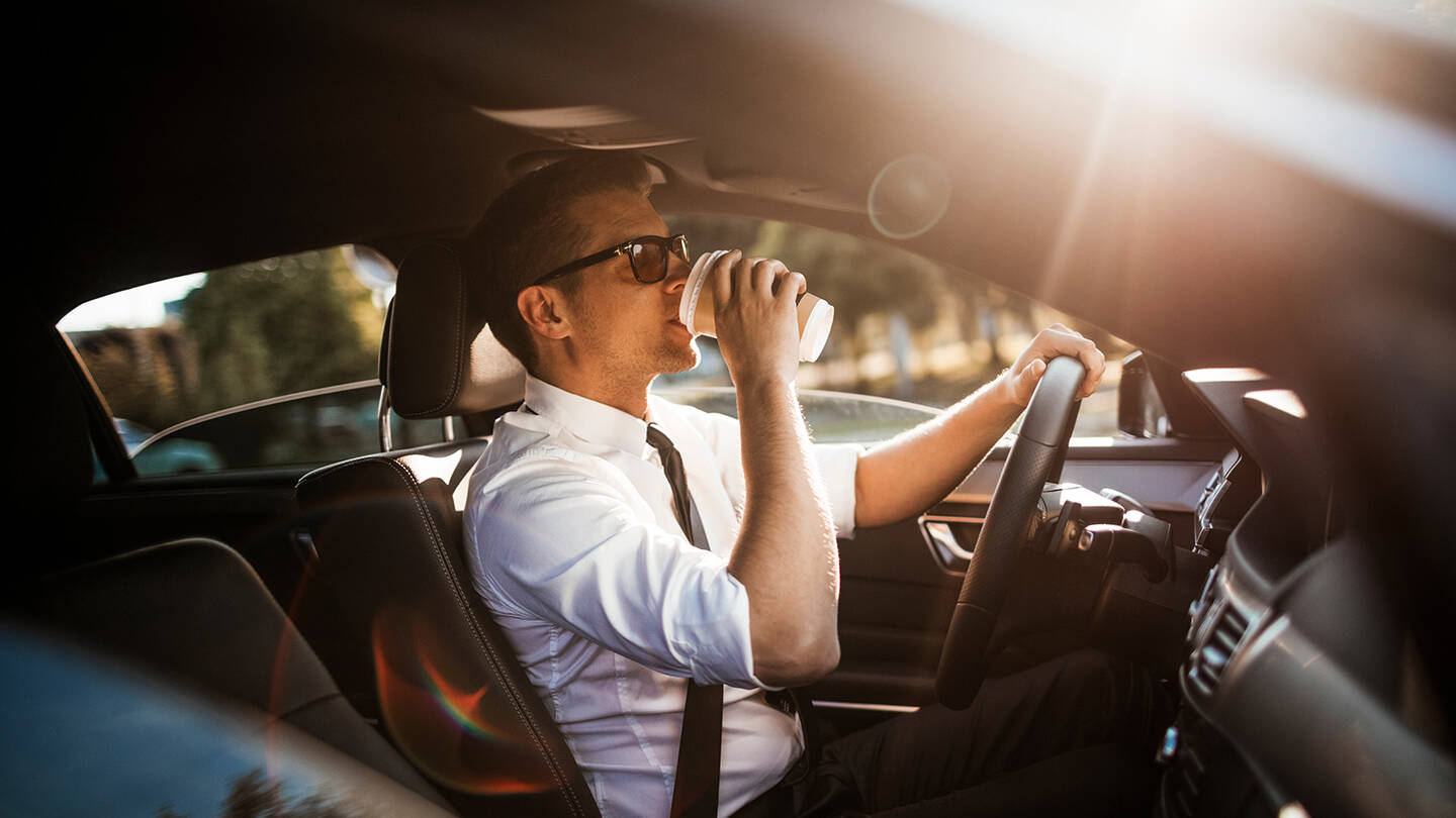 communter drinking coffee in car in traffic